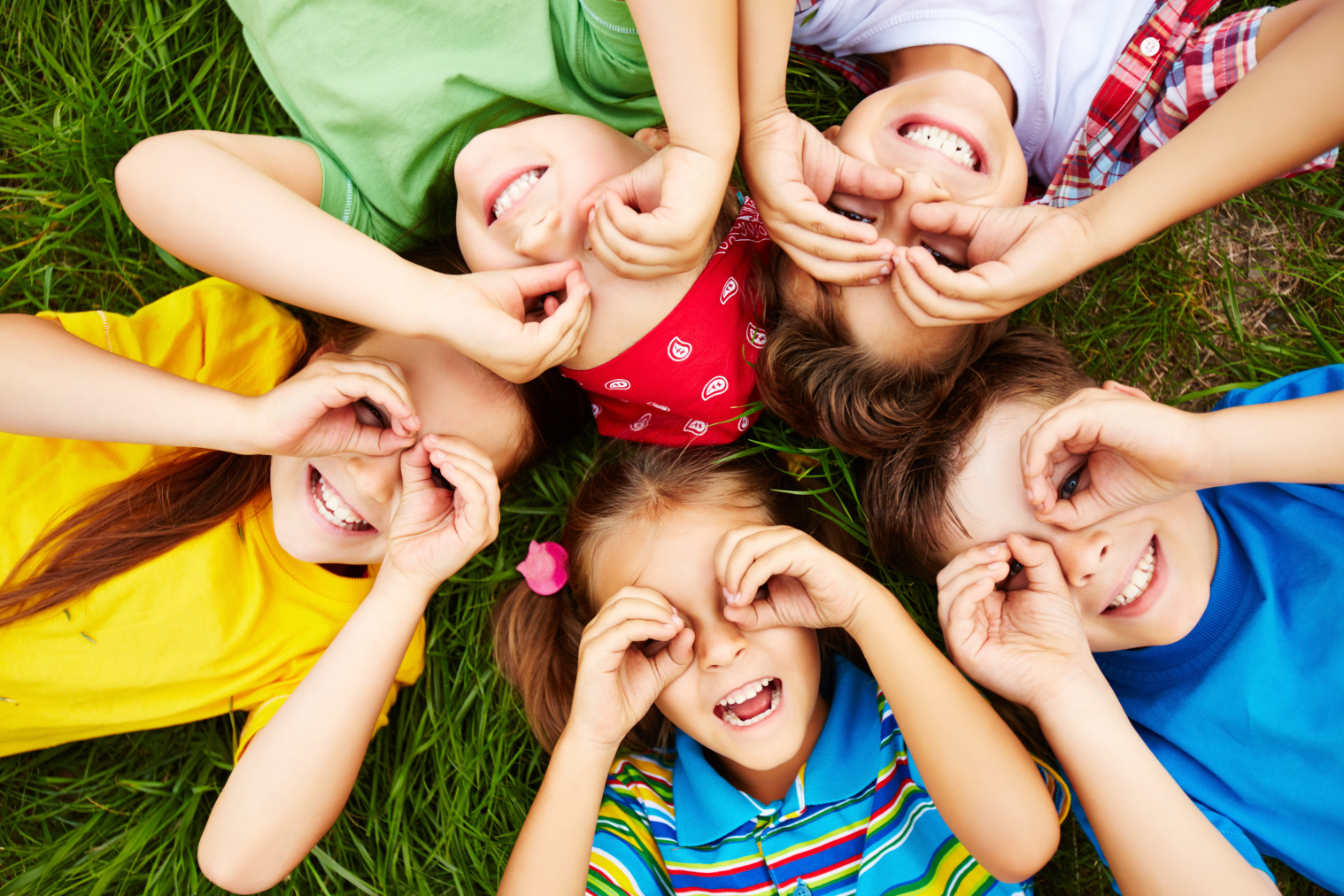 Mehrere Kinder liegen auf einer Wiese auf dem Rücken und formen mit den Händen eine Brille.