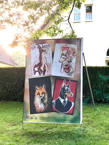 Eine Plakatleinwand zeigt Kunstwerke eines Rehs, eines Fuchses und eines Hundes